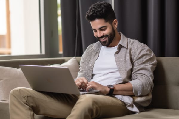 Best Certifications to Get in IT : A Guide to Most Valuable Certs for Professionals. A man smiling and working on his laptop while comfortably lounging on a couch.